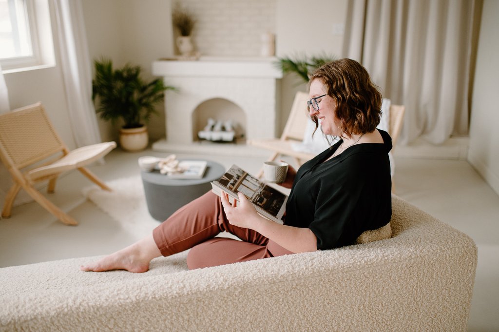 Samantha relaxes on a couch while reading a book in a staged headshot.